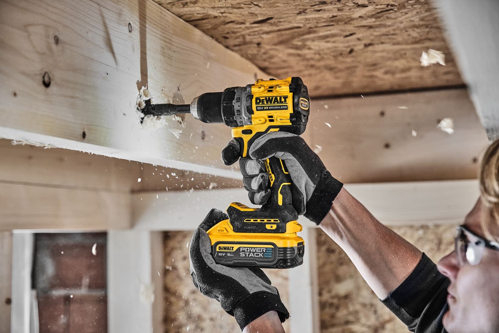 Persona perfora viga de madera con taladro DEWALT, usando guantes y gafas de seguridad.