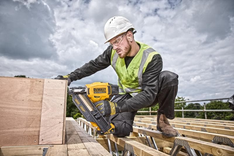 Persona usa una clavadora DEWALT DCN930N en madera en obra exterior, llevando equipo de seguridad.