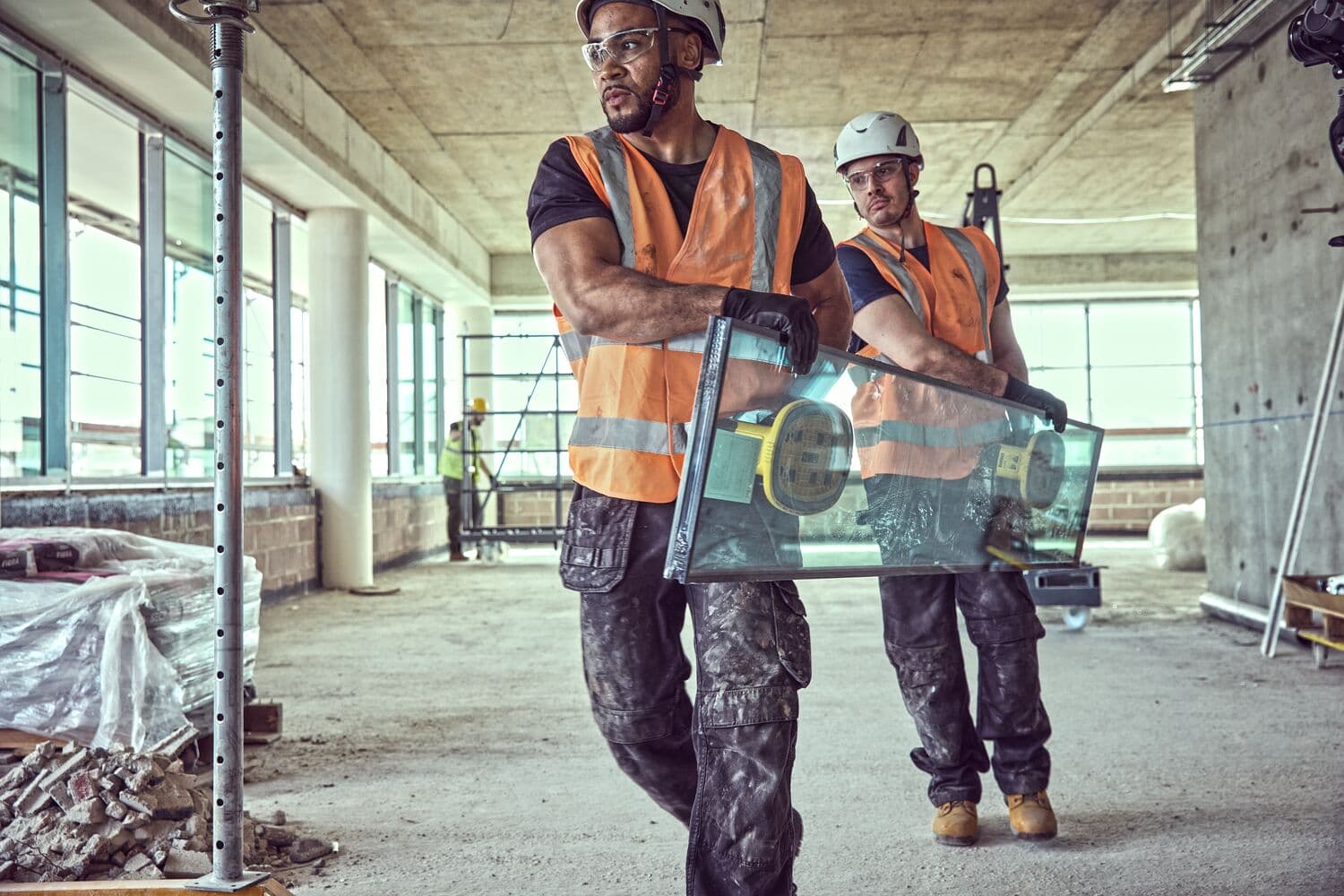 Dos trabajadores llevan vidrio con herramientas de succión en una obra.
