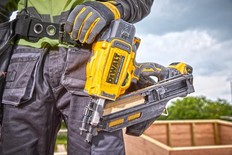 Persona sostiene una clavadora DEWALT DCN930N, con guantes y equipo de trabajo en una obra al aire libre.