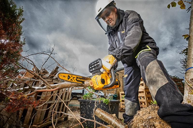 Persona con equipo de seguridad usa una motosierra DEWALT para cortar ramas afuera en un día nublado.
