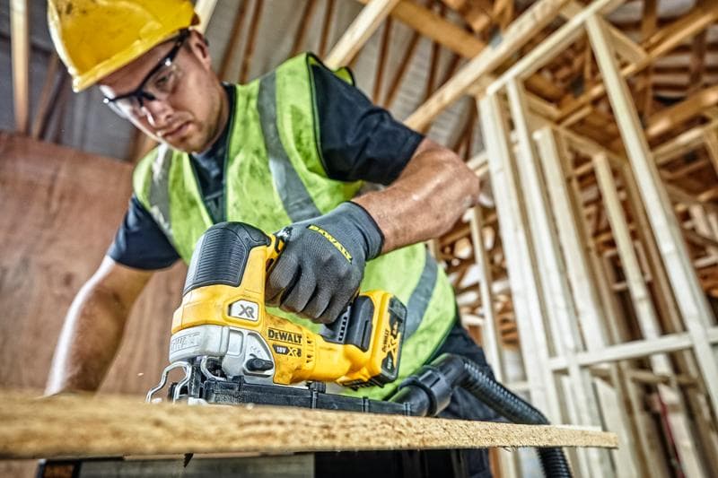 Sierra DEWALT DCS334P2 corta madera en obra, operario usando equipo de seguridad.