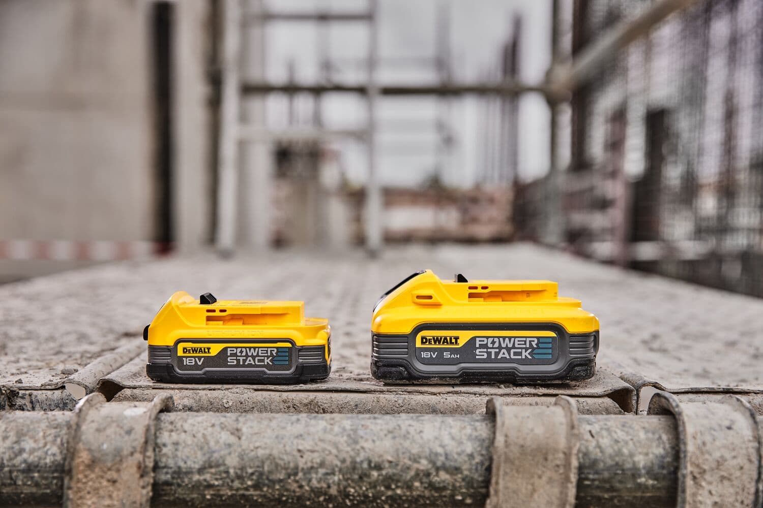 Dos baterías DEWALT 18V POWERSTACK sobre una superficie de obra, fondo industrial desenfocado.