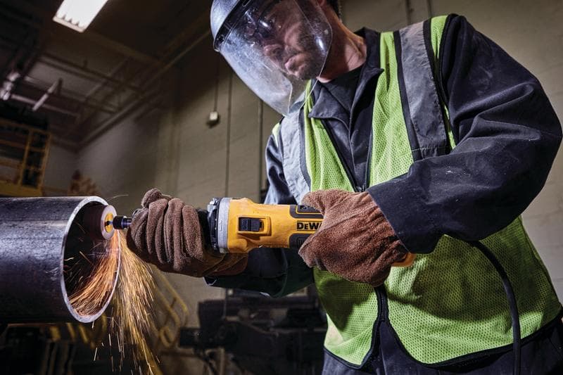 Trabajador usa amoladora DEWALT para cortar tubo metálico, chispas, guantes y equipo de seguridad.