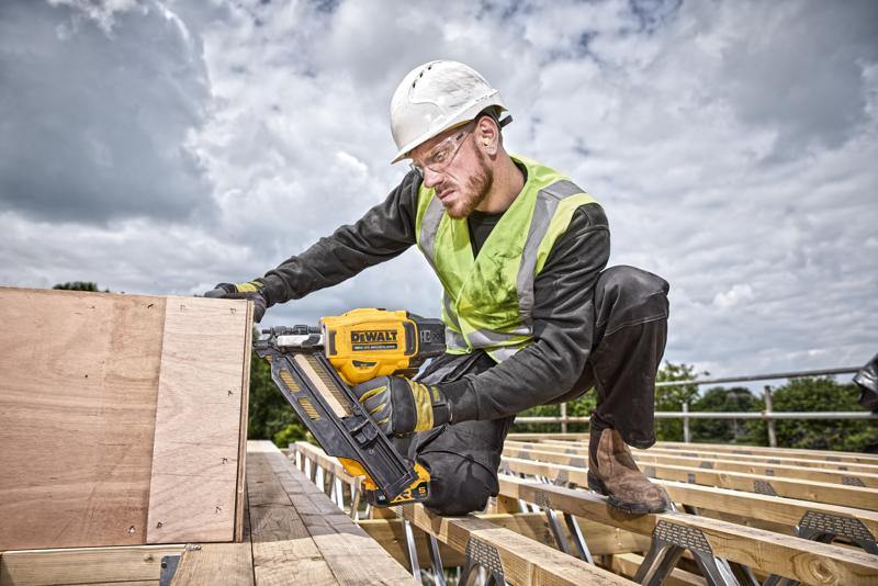Persona usa una clavadora DEWALT DCN930N en madera en obra exterior, llevando equipo de seguridad.