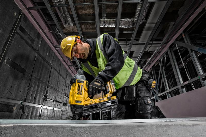 Trabajador usa la clavadora DEWALT DCN890P2 en construcción, con casco y chaleco de seguridad.