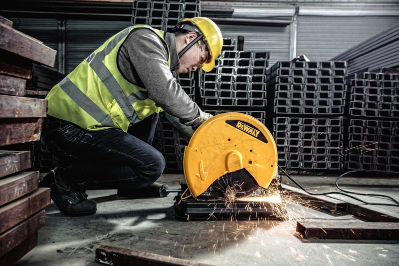 Una persona con equipo de seguridad opera una sierra de corte de metal DEWALT, modelo D28730, para cortar barras metálicas en un entorno industrial. Saltan chispas de la zona de corte.