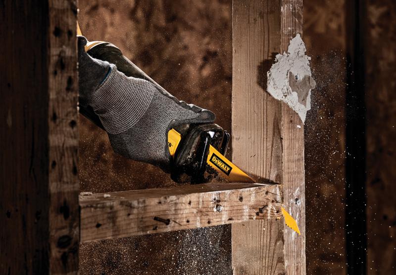 Primer plano de una mano con un guante gris usando una sierra recíproca DEWALT para cortar una viga de madera, con aserrín volando en el aire.