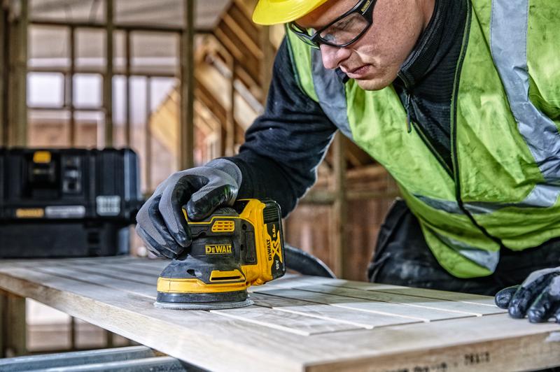 DEWALT DCW210, DCW210D1 lijadora en uso sobre madera, obra, persona con guantes y chaleco de seguridad.