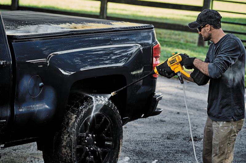 Una persona está usando una hidrolavadora inalámbrica DEWALT DCPW550B para limpiar la rueda y el lateral de una camioneta negra al aire libre.