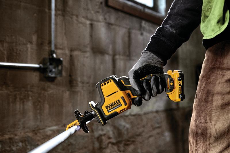 Mano enguantada sostiene sierra recíproca DEWALT DCS312D2 cortando tubo metálico en interior.