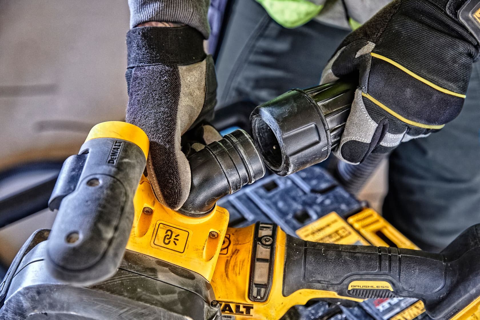 Manos con guantes conectan una manguera a una herramienta amarilla DEWALT en primer plano.