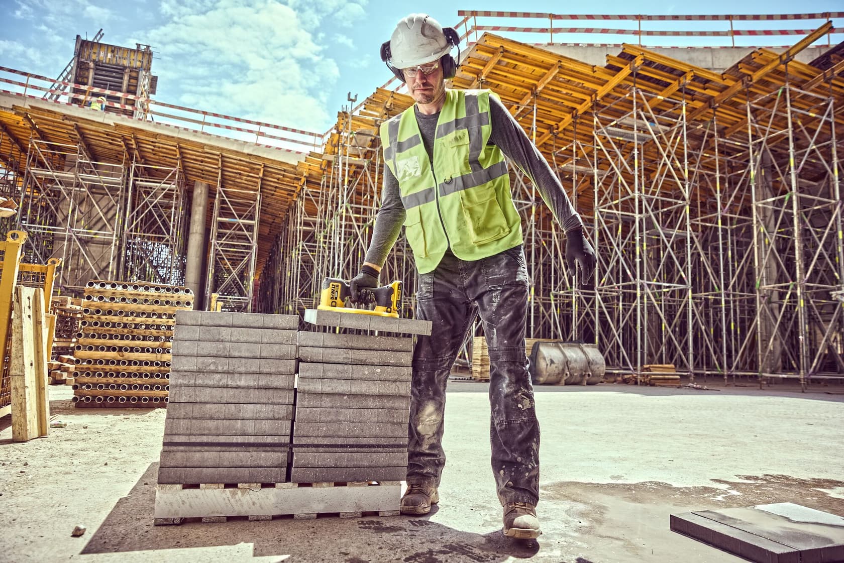 Trabajador levanta una losa de cemento con herramienta DEWALT, lleva equipo de seguridad y chaleco.