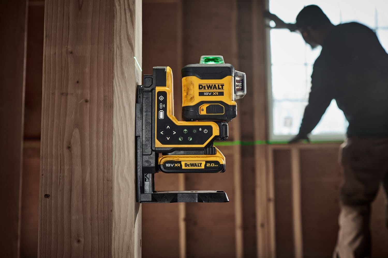 Nivel láser DEWALT en viga de madera, proyecta líneas verdes, persona trabajando al fondo.