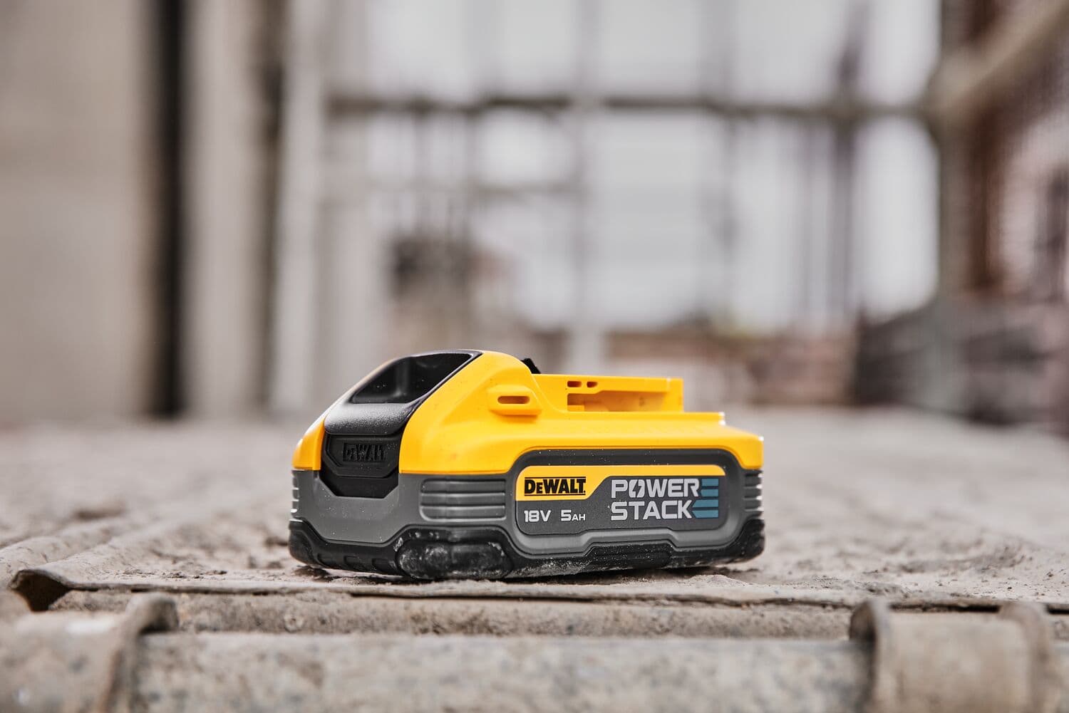 Batería DEWALT POWERSTACK 18V 5Ah sobre superficie de concreto en entorno industrial.